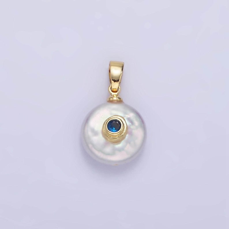 May include: A white pearl pendant with a gold setting and a small blue gemstone in the center.