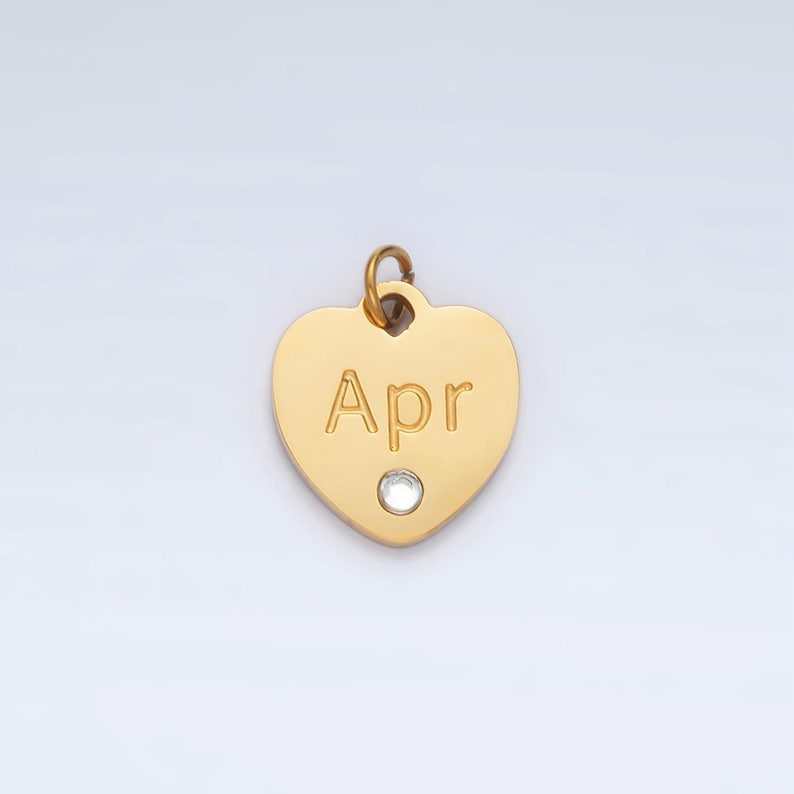 May include: Gold heart-shaped charm with a clear rhinestone and the word "Apr" engraved on it.