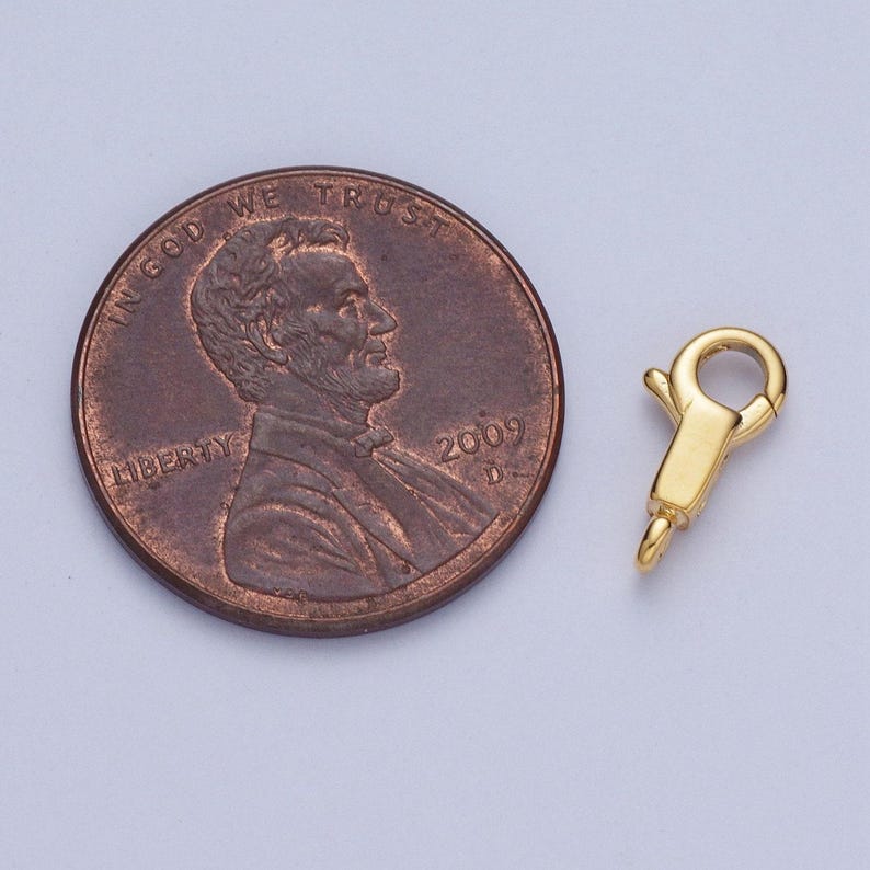 May include: Gold-toned metal clasp for jewellery making, shown next to a UK penny for size comparison.
