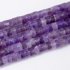 May include: Close-up of strands of amethyst gemstone beads. The beads are cylindrical with a flat, rectangular shape. The color of the beads ranges from light to dark purple. The beads are strung together, creating a textured surface.
