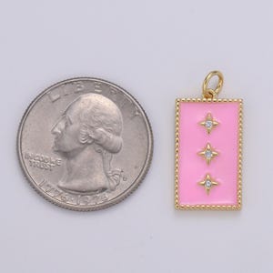 May include: A gold charm with a pink enamel rectangle and three gold stars with clear rhinestones. The charm is about the size of a US quarter.