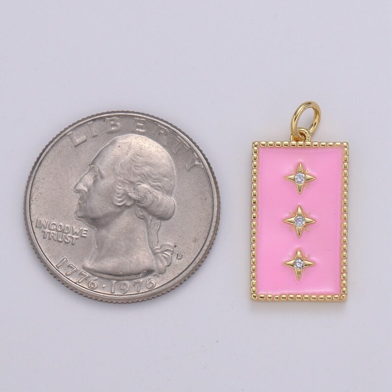 May include: A gold charm with a pink enamel rectangle and three gold stars with clear rhinestones. The charm is about the size of a US quarter.