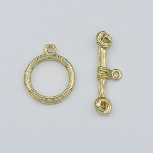May include: Gold-toned metal clasp with a round ring and a bar with a loop. The clasp is designed for jewelry making.