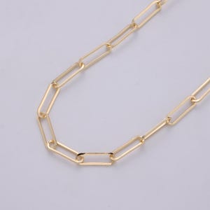 Puede incluir: Un collar de cadena de clip de papel de color dorado. El collar presenta una serie de eslabones rectangulares conectados entre sí. La cadena se muestra sobre un fondo claro.