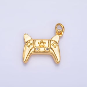 May include: A gold-colored pendant in the shape of a video game controller. The controller has a paw print design in the center and small, round embellishments. Two clear gems are set on the controller. The pendant has a loop for attaching to a chain.