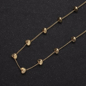 May include: A gold chain necklace with round, slightly flattened gold beads. The necklace is on a black background.