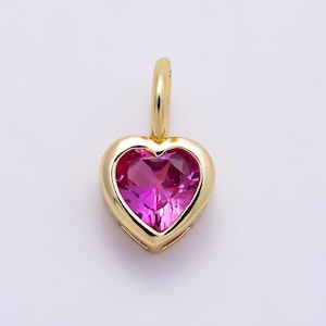 May include: A gold heart-shaped pendant featuring a faceted, vibrant pink gemstone set in a polished gold frame. The pendant includes a small, rounded gold bail at the top for attachment, showcasing a clean, symmetrical design with a bright finish.