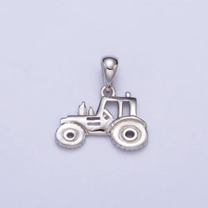 May include: A silver-colored tractor pendant with detailed features, including wheels, a cab, and exhaust pipes. The pendant has a loop at the top for attaching to a chain or bracelet. The tractor is a miniature replica.
