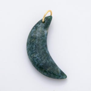 Op de afbeelding: Een maanvormige hanger met een goudkleurige lus. De hanger is een gevlekte groen en blauwe steen. De steen heeft een glad, gepolijst oppervlak. De hanger is waarschijnlijk voor een ketting of andere sieraden.