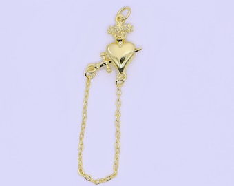May include: A gold-colored pendant featuring a heart pierced by an arrow, with a crown and cross detail. A delicate chain extends from the heart, creating a loop. The pendant is likely for jewelry.