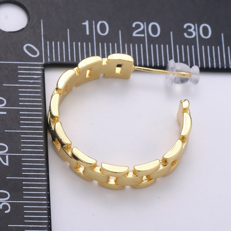 May include: Gold-toned hoop earrings with a chain-link design. The earrings are approximately 2 cm in diameter.