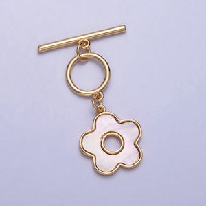 May include: Gold-tone toggle clasp with a white flower charm. The flower has a gold-tone outline and a small circle in the center.