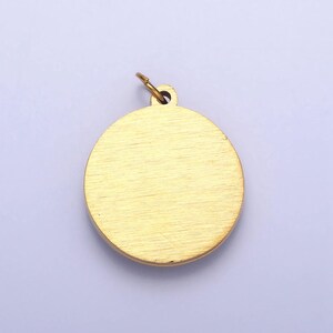 May include: A gold-colored round pendant with a smooth, brushed finish. The pendant has a loop at the top for attaching a chain.