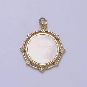 May include: A gold pendant with a round, white mother-of-pearl inlay surrounded by a gold frame with small clear stones.