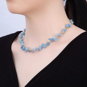May include: A delicate necklace featuring light blue, irregularly shaped gemstones interspersed with small gold-colored beads. The necklace is worn around the neck, showcasing the natural beauty of the stones. The necklace is a stylish accessory.
