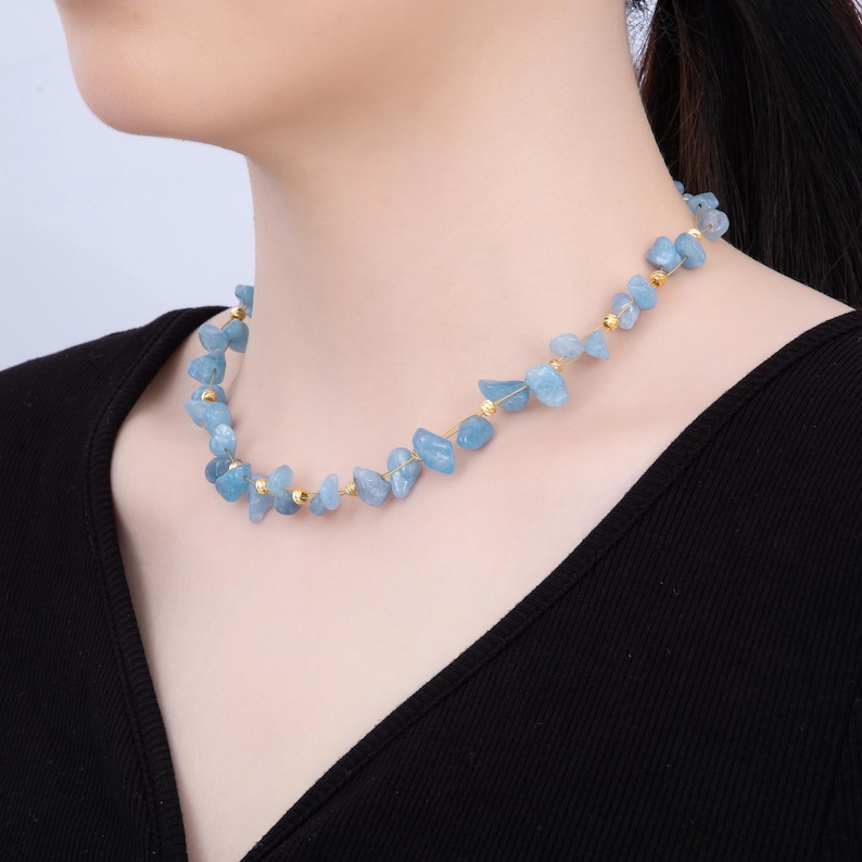 May include: A delicate necklace featuring light blue, irregularly shaped gemstones interspersed with small gold-colored beads. The necklace is worn around the neck, showcasing the natural beauty of the stones. The necklace is a stylish accessory.