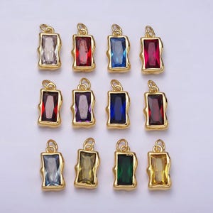 Puede incluir: Doce colgantes de tono dorado con piedras de vidrio de diferentes colores. Cada colgante presenta una piedra rectangular de forma ligeramente irregular.