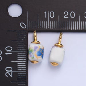 May include: Two white ceramic square beads with gold accents and floral patterns. The beads have a gold loop at the top for hanging.