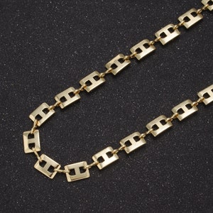 Puede incluir: Un collar de cadena de oro con un diseño de eslabón cuadrado. La cadena está hecha de metal y tiene un acabado pulido.