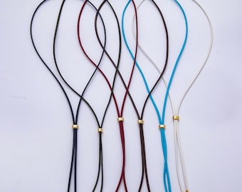 May include: A collection of six leather bolo ties in various colors, including black, navy, burgundy, brown, turquoise, and white. Each tie features a gold-colored metal accent and tips. The ties are arranged against a white background.