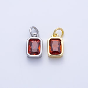 May include: Two rectangular pendants with a red gemstone centre. One pendant has a silver-coloured frame and loop, while the other has a gold-coloured frame and loop. The gemstones are a deep red colour, set against a white background.