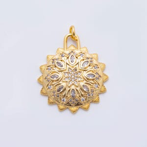 May include: A gold-colored pendant with a sunburst design. The pendant features a central starburst pattern surrounded by clear, oval-shaped stones and smaller, round stones. The pendant has a loop at the top for attaching to a chain.