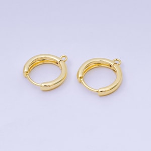 May include: Two gold-colored hoop earrings. Each earring has a rounded, hollow design with a small loop at the top for attachment. The earrings are made of a shiny, metallic material, reflecting light.