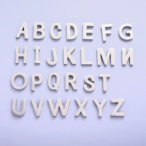 Peut inclure: Breloques en forme de lettres de l'alphabet en argent, de A à Z, disposées en trois rangées sur un fond violet clair.