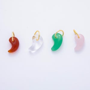 May include: Four gemstone pendants in a row, each with a gold-colored loop. The pendants are in shades of red, clear, green, and pink. The pendants have a curved, comma-like shape, and are set against a white background.