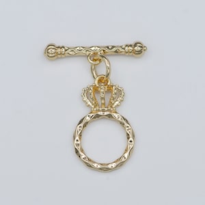 May include: Gold-toned metal toggle clasp with a crown charm and a textured ring.