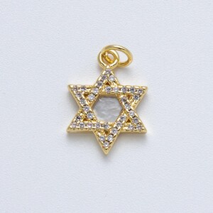 May include: A gold-toned Star of David pendant featuring a central hexagonal cutout and a border encrusted with small, clear, sparkling stones. The charm includes a small circular jump ring at the top for attachment to a chain or necklace.