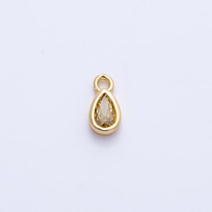 May include: A gold-colored teardrop-shaped pendant with a light brown gemstone. The pendant has a small loop at the top for attaching to a chain or other jewelry. The gemstone is set within a gold bezel.