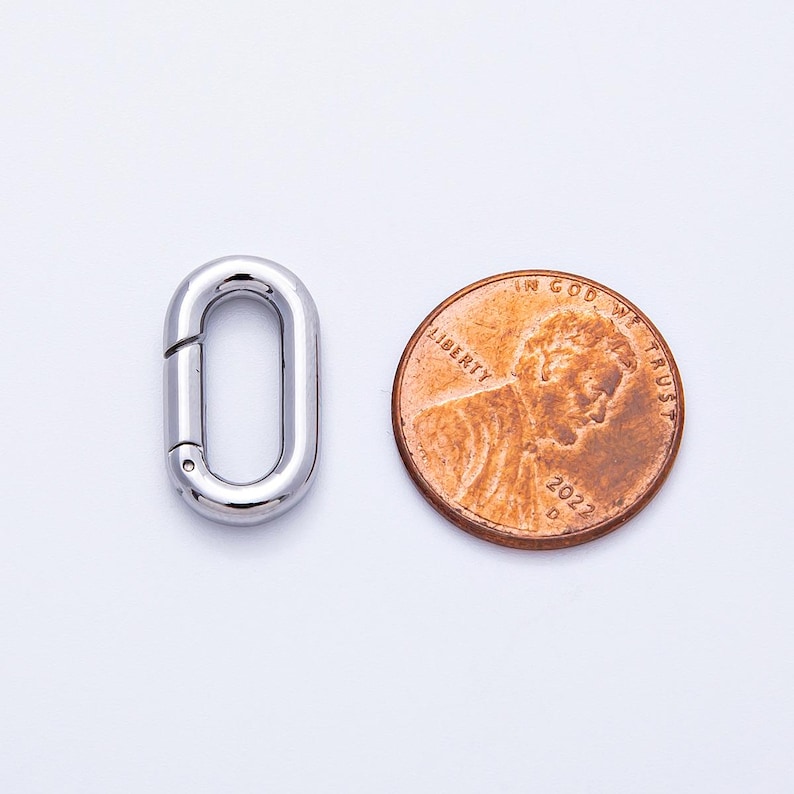 以下が含まれることがあります： 光沢のある銀色の楕円形の留め金と、米国のペニー。留め金にはヒンジ付きの開口部があります。ペニーには人物の横顔と「Liberty」と「In God We Trust」という言葉、そして2022年が示されています。