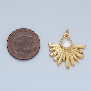 May include: Gold-colored sunburst pendant with a circular, pearlescent center. The pendant has a detailed, textured design and a small loop for attaching to a chain. A U.S. one-cent coin is next to the pendant for size comparison.
