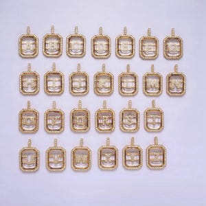 May include: A set of 26 gold-toned pendants, each featuring a different letter of the alphabet, set with clear cubic zirconia stones. The pendants are in a square shape with a slightly rounded edge.