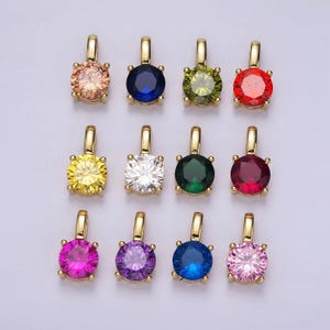 May include: Twelve gold pendants with round, colorful gemstones. The pendants are arranged in three rows of four. The gemstones are red, green, blue, purple, pink, yellow, white, and orange.