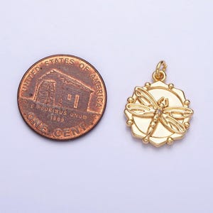 May include: Gold-toned pendant featuring a detailed dragonfly design with a clear rhinestone in the center. The pendant is approximately the size of a US penny.