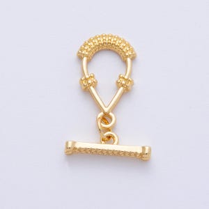 May include: A gold-colored toggle clasp for jewelry making. The clasp features a textured, rounded top, a V-shaped connecting piece, and a horizontal bar. The design is symmetrical and suitable for necklaces or bracelets.