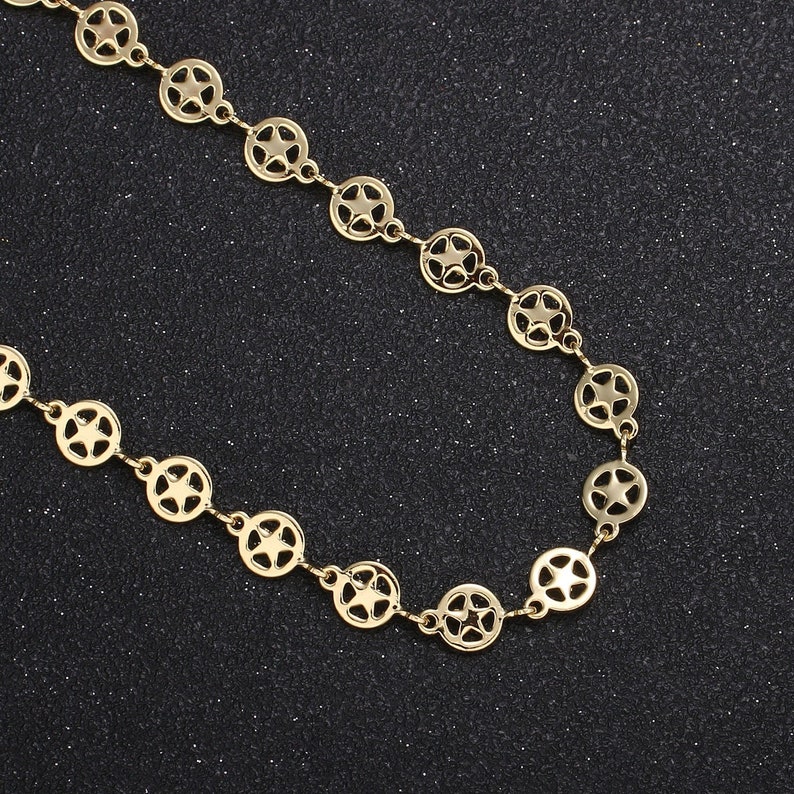 May include: Gold-colored necklace featuring a repeating pattern of open circles with star cutouts. The necklace is displayed against a dark, textured background, highlighting its metallic sheen. A delicate piece of jewelry.