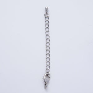 May include: A silver-colored necklace extender with a lobster clasp at the bottom and a small loop at the top. The extender is made of small, connected chain links. The background is plain white.