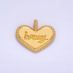 May include: Gold heart-shaped pendant with a rope-like border and the word "honey" inscribed in a cursive font.