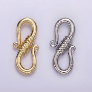 May include: Two metal clasps, one gold and one silver, with a unique twisted design. The clasps are shaped like an 'S' and have a hook on one end.