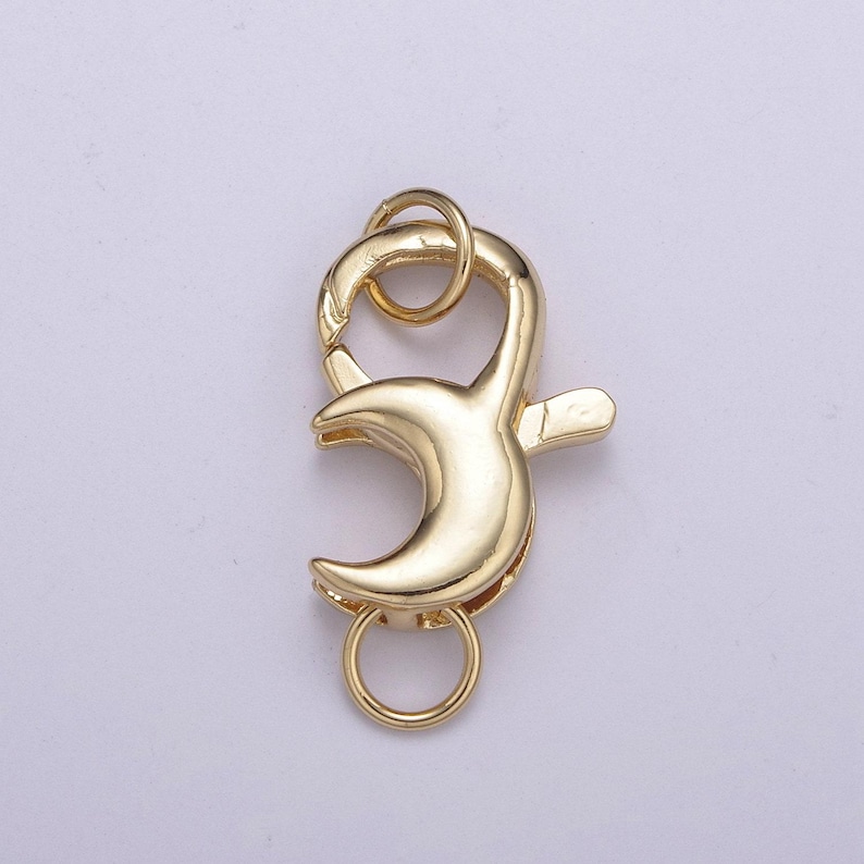 May include: Gold-toned metal clasp with a crescent moon design. The clasp has two rings for attaching to a necklace or bracelet.
