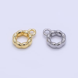 Puede incluir: Dos colgantes de joyería de metal. Uno es de color dorado, el otro plateado. Cada colgante es un anillo de formas redondeadas conectadas con un pequeño lazo en la parte superior para sujetarlo a la joyería. Los colgantes están sobre un fondo claro.