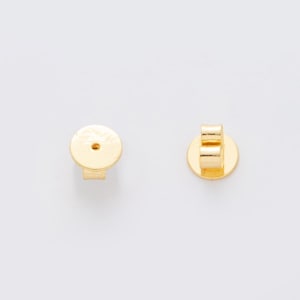 Peut inclure: Deux fermoirs de boucles d'oreilles dorés sur fond blanc. L'un est un disque plat avec une tige, l'autre est de type papillon. Les fermoirs sont en métal brillant.