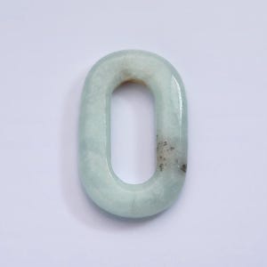 May include: A light blue oval-shaped stone with a hole in the center. The stone has a smooth, polished surface and a mottled pattern.