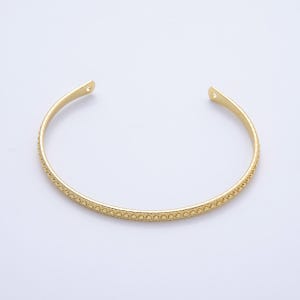 May include: A gold-colored cuff bracelet with a dotted pattern along the front. The open-ended bracelet has a smooth, polished finish and is designed to slip over the wrist. The bracelet is a simple, elegant piece of jewelry.