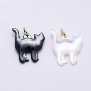 May include: Two cat-shaped charms made of iridescent shell material. One charm is dark charcoal gray with a glossy finish, and the other is white with a pearlescent sheen. Each charm features a small gold-toned metal jump ring at the top.