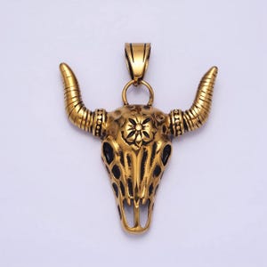 May include: Gold-toned bull skull pendant with black detailing and a floral design on the forehead. The pendant has a loop at the top for attaching to a chain.