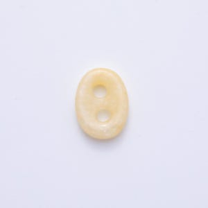 May include: Oval-shaped, pale yellow button with two holes. The button has a smooth, polished surface and a slightly translucent appearance. The button is set against a white background.